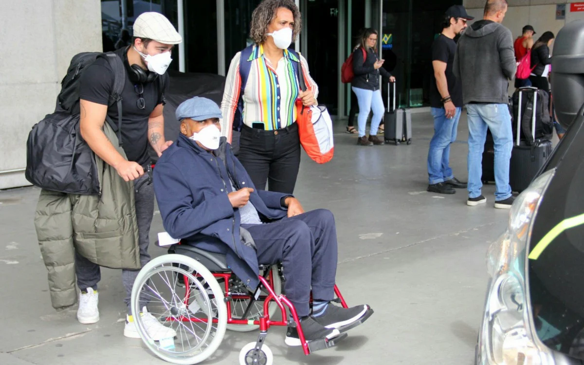  Em cadeira de rodas, Milton Nascimento desembarca em aeroporto do Rio